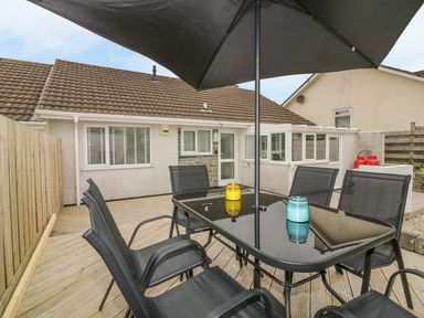 An outdoor patio with a black table set and umbrella on wooden decking at Dune Haven in Goonhavern near Perranporth