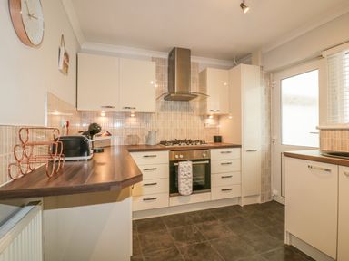 A kitchen with cream cabinets dark countertops a gas stove an oven and a door with frosted glass at Dune Haven in Goonhavern near Perranporth