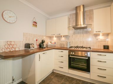 A kitchen with white cabinets a stainless steel oven and cooker hood and appliances on the counter at Dune Haven in Goonhavern near Perranporth