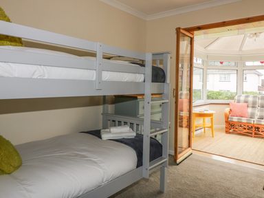 A bedroom with a grey bunk bed and folded towels with a view into a sunroom with wicker furniture at Dune Haven in Goonhavern near Perranporth