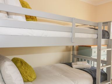A bedroom with a grey bunk bed a green dresser and yellow pillows at Dune Haven in Goonhavern near Perranporth