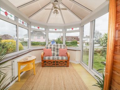 A conservatory with a wicker loveseat with cushions a ceiling fan and a yellow side table at Dune Haven in Goonhavern near Perranporth
