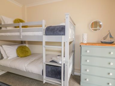 A bedroom with a gray bunk bed and a mint green dresser with a round mirror and a model boat at Dune Haven in Goonhavern near Perranporth
