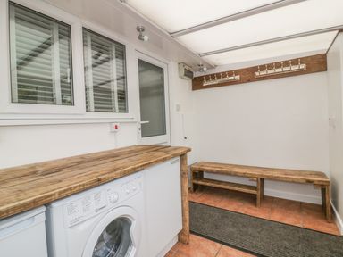 A utility room with a washing machine wooden countertop wooden bench coat hooks on the wall and tiled floor at Dune Haven in Goonhavern near Perranporth