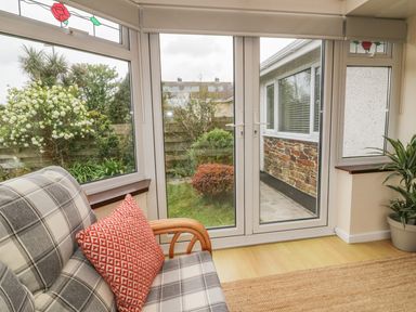A seating area with a plaid patterned sofa and red cushion near glass doors overlooking a garden at Dune Haven in Goonhavern near Perranporth