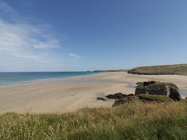 A wide sandy beach with rocky formations and grassy dunes under a clear sky at Dune Haven in Goonhavern near Perranporth