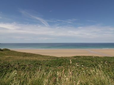 A beach with sand and ocean beyond grassy dunes at Dune Haven in Goonhavern near Perranporth