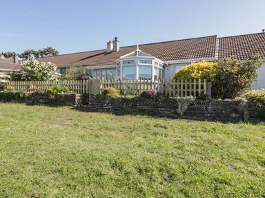 Exterior of a single-story house with a brown tiled roof garden with shrubs picket fence and grass lawn at Dune Haven in Goonhavern near Perranporth