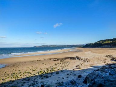A wide sandy beach with sparse seaweed and rocks along the shore and hills in the background at Cysgod Y Capel in Benllech