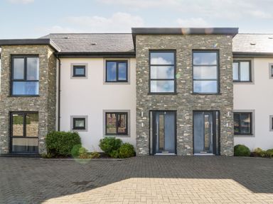 A modern two-story stone and white facade building with numbered blue front doors and windows at Cysgod Y Capel in Benllech