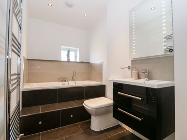 A bathroom with a bathtub toilet sink with cabinet and mirror at Cysgod Y Capel in Benllech