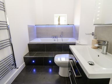 A bathroom with a built-in bathtub black tiled steps a white sink and a toilet at Cysgod Y Capel in Benllech