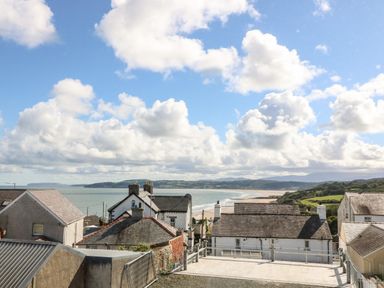A coastal village with rooftops, a beach, sea, hills under a cloudy sky at Cysgod Y Capel in Benllech