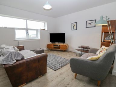 A living room with two sofas a television on a wooden stand and a floor lamp at Cysgod Y Capel in Benllech