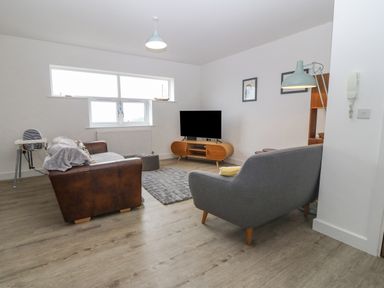 A living room with two sofas a television on a wooden stand a highchair and a floor lamp at Cysgod Y Capel in Benllech