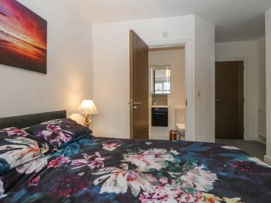 A bedroom with a floral bedspread a bedside lamp and an open door showing a bathroom at Cysgod Y Capel in Benllech