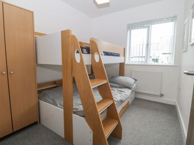 A bedroom with wooden bunk beds next to a wooden wardrobe and a window at Cysgod Y Capel in Benllech