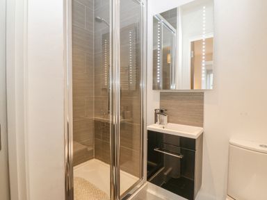 A bathroom with a glass shower enclosure a sink with cabinet below and a toilet at Cysgod Y Capel in Benllech