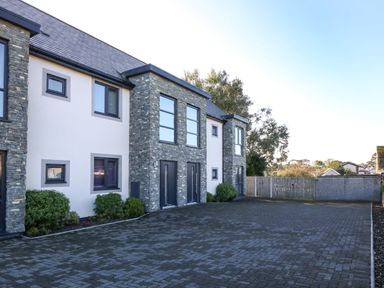 A paved driveway in front of a modern two story house with stone and white exterior walls and several windows at Cysgod Y Capel in Benllech