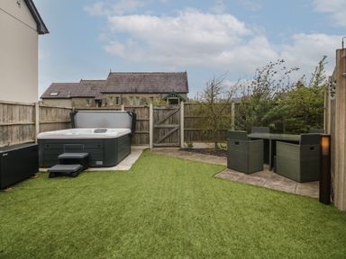A backyard with a hot tub on a concrete pad a dining table with four chairs on a tiled area and a wooden fence surrounding the space at Cysgod Y Capel in Benllech