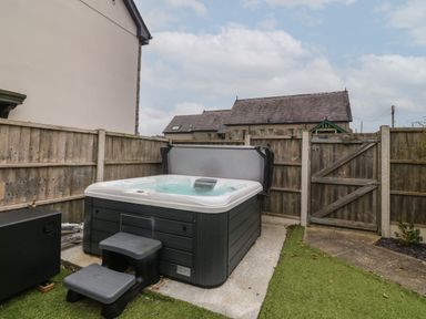 An outdoor hot tub with steps next to a wooden fence and gate at Cysgod Y Capel in Benllech