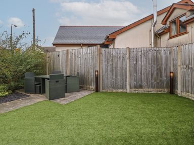 A garden with artificial grass a patio dining set and string lights on a wooden fence at Cysgod Y Capel in Benllech