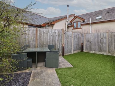 A fenced backyard with a patio dining set and artificial grass at Cysgod Y Capel in Benllech