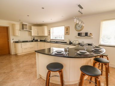 A kitchen with a curved black countertop island and stools with plates and glasses at Cadwgan in Aberporth