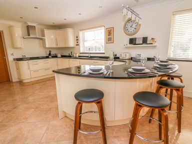 A kitchen with a curved island countertop with stools and place settings at Cadwgan in Aberporth