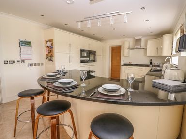 A kitchen with a curved black countertop island set with plates and glasses and three stools at Cadwgan in Aberporth