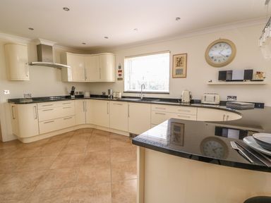 A kitchen with curved white cabinets black countertops a window a wall clock and small appliances at Cadwgan in Aberporth