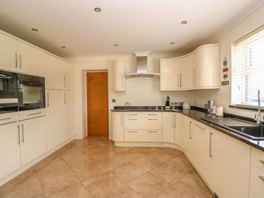 A kitchen with cream cabinets black countertops built in oven microwave a window and a wooden door at Cadwgan Aberporth