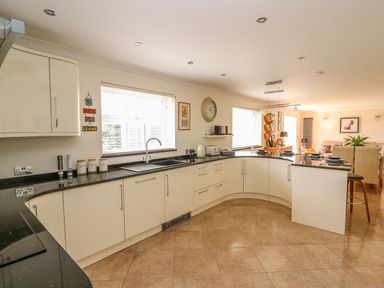 A kitchen with white cabinets black countertops and a dining area in the background at Cadwgan Aberporth