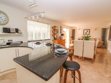 A kitchen with a black countertop and bar stools next to a dining area with chairs and a sofa at Cadwgan in Aberporth