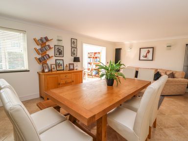 A dining room with a wooden table and white chairs a wooden sideboard with framed photos and a plant on the table at Cadwgan in Aberporth