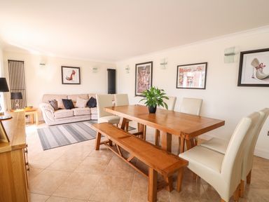 A dining room with a wooden table bench and chairs and a sofa with cushions at Cadwgan in Aberporth
