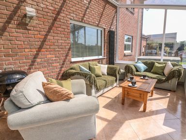 A sunroom with three sofas a wooden coffee table with cups and saucers and a brick wall at Cadwgan in Aberporth