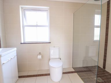 A bathroom with a white toilet under a window a white sink cabinet and a glass shower area at Cadwgan in Aberporth