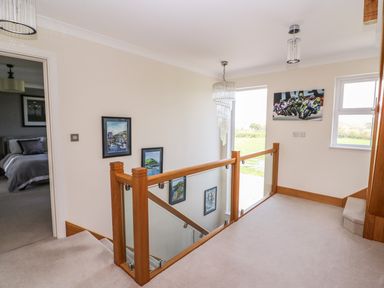 A stairwell with wooden and glass railing and paintings on the wall in the hallway of Cadwgan in Aberporth