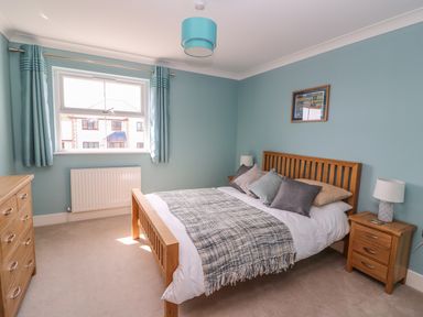 A bedroom with a wooden bed frame a dresser and bedside tables with lamps at Cadwgan in Aberporth