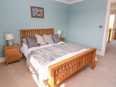 A bedroom with a wooden bed frame two bedside tables with lamps a framed picture on a blue wall and an open door at Cadwgan in Aberporth