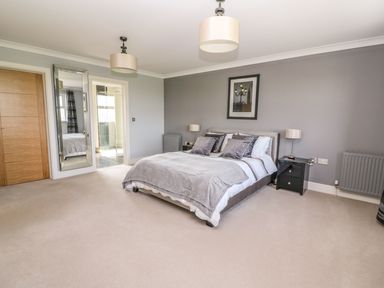 A bedroom with a double bed bedside tables lamps a framed picture a full length mirror and an ensuite bathroom at Cadwgan in Aberporth
