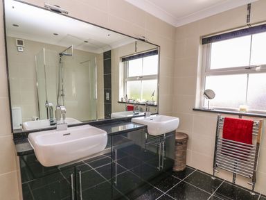 A bathroom with two sinks a large mirror a shower a window and a towel rack with a red towel at Cadwgan in Aberporth