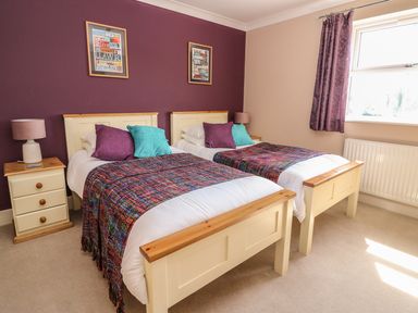 A bedroom with two single beds with colorful throws and pillows next to a window with purple curtains at Cadwgan in Aberporth