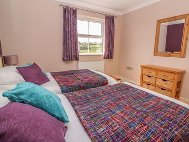 A bedroom with two single beds with colorful blankets purple and turquoise cushions and a wooden dresser with a mirror at Cadwgan in Aberporth