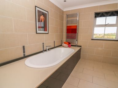 A bathroom with a built in bathtub towels on the counter towel warmer and a window at Cadwgan in Aberporth
