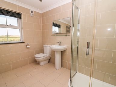 A bathroom with a toilet pedestal sink corner shower and window at Cadwgan in Aberporth
