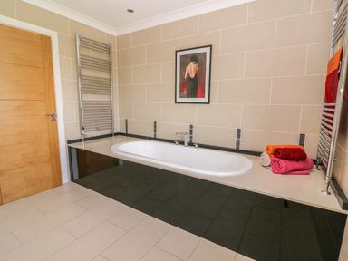 A bathroom with a built-in bathtub towels on the side and a framed picture above at Cadwgan in Aberporth