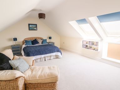 A bedroom with a bed blue bedding bedside tables and a wicker armchair under skylight windows at Cadwgan in Aberporth