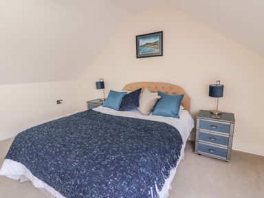 A bedroom with a bed with blue and white bedding two bedside tables with lamps and a painting above the bed at Cadwgan in Aberporth